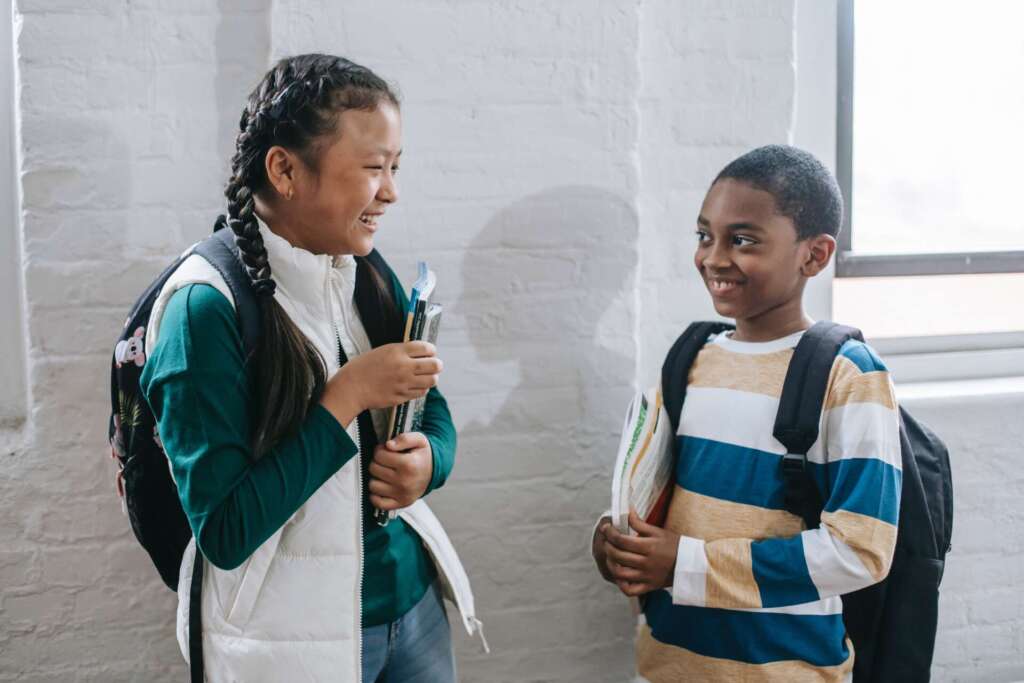 A girl and boy stand smiling at each other while holding their books and wearing backpacks, nonverbal learning disorder
