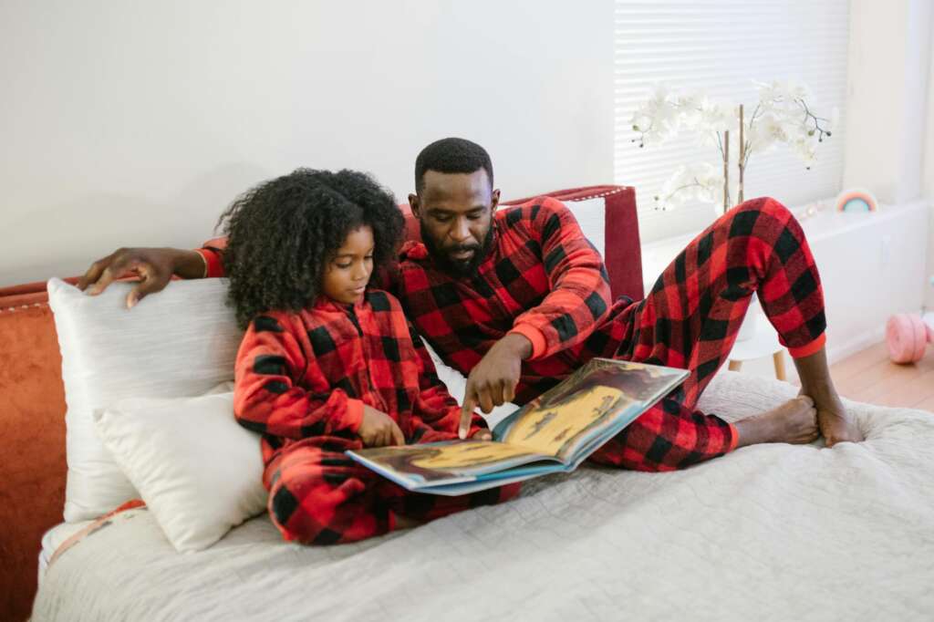 father reading book with daughter on bed; Children's Books about Autism
