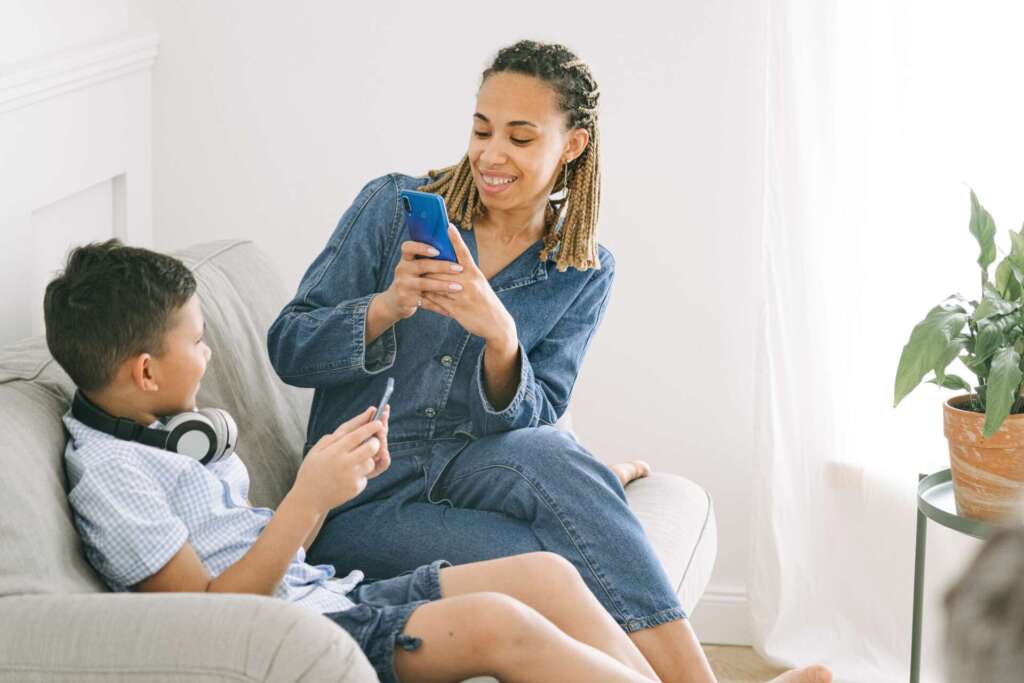 A woman sits on a sofa while taking a picture of a boy with a mobile phone; sharenting