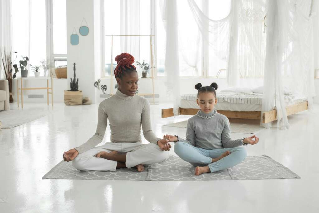 Young black mother practicing yoga with daughter in light bedroom; Empower kids to make the right choices